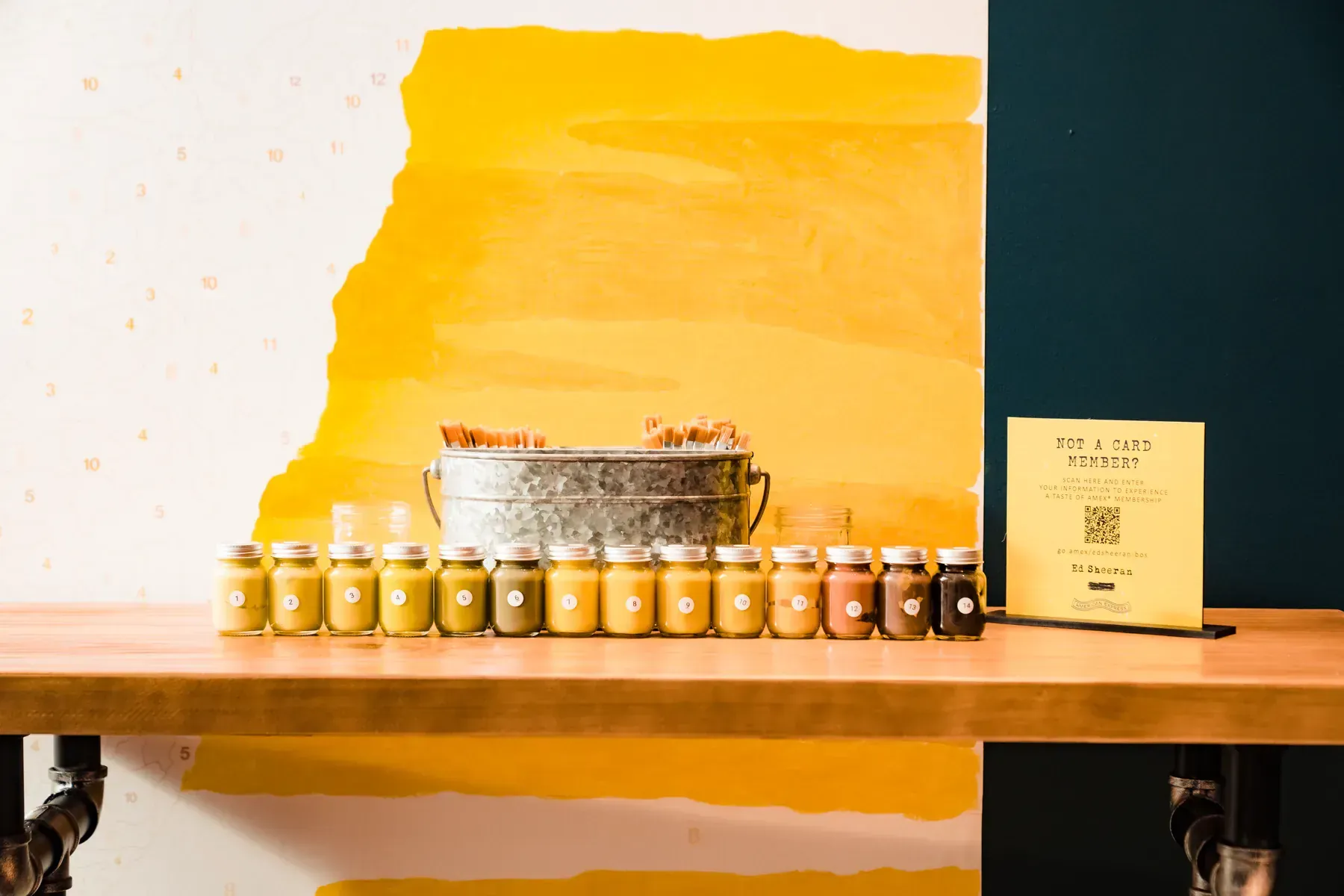Numbered yellow and earth-tone paints arranged in front of the Ed Sheeran paint-by-number mural