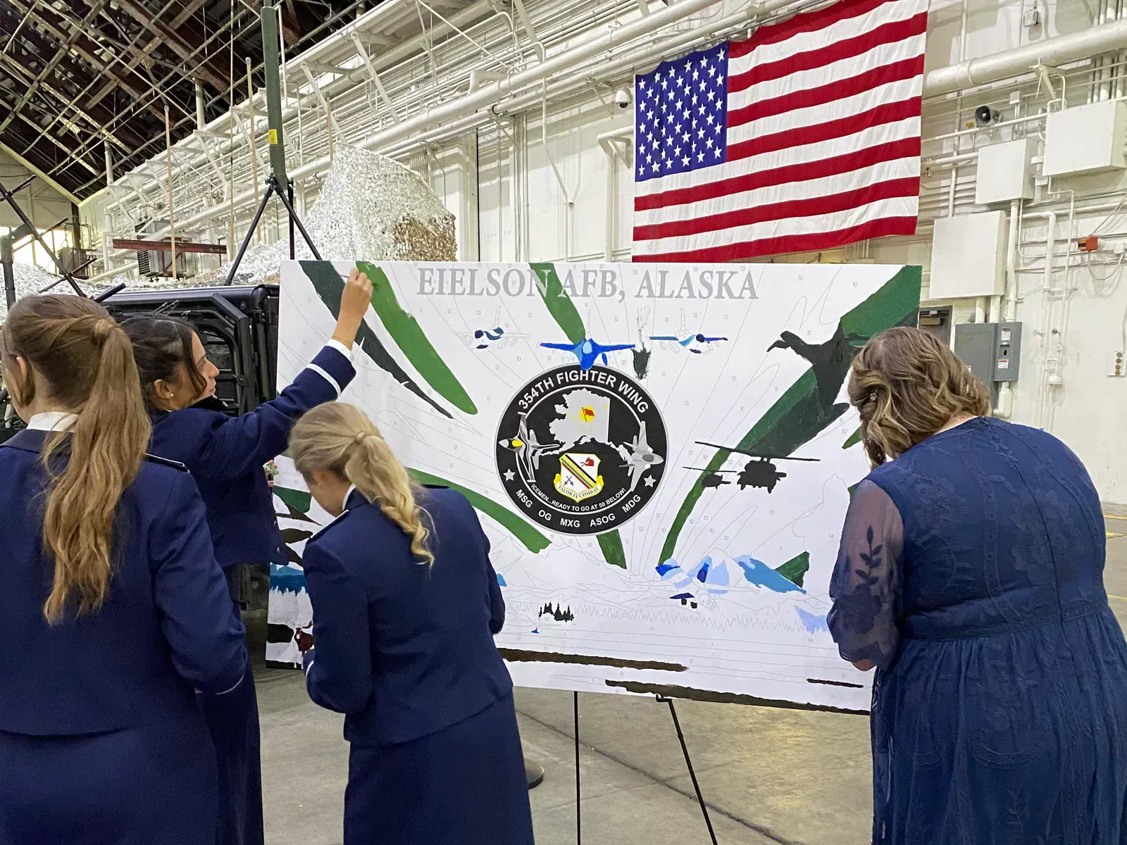 Four Air Force Ball guests painting an Eielson Air Force Base paint-by-number mural beneath an American flag