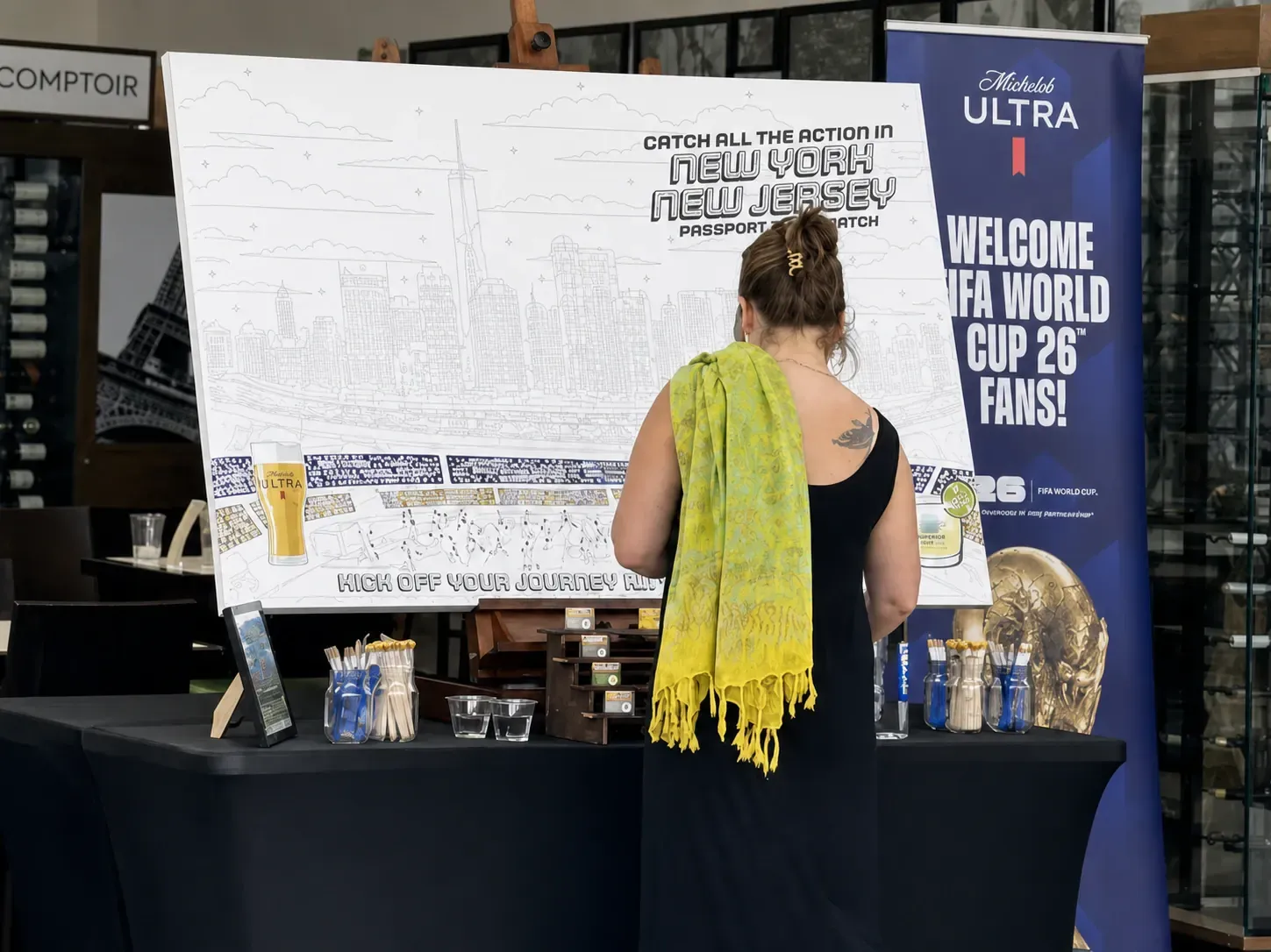 Guest painting a New York New Jersey World Cup paint-by-number mural beside a Michelob ULTRA banner at JFK