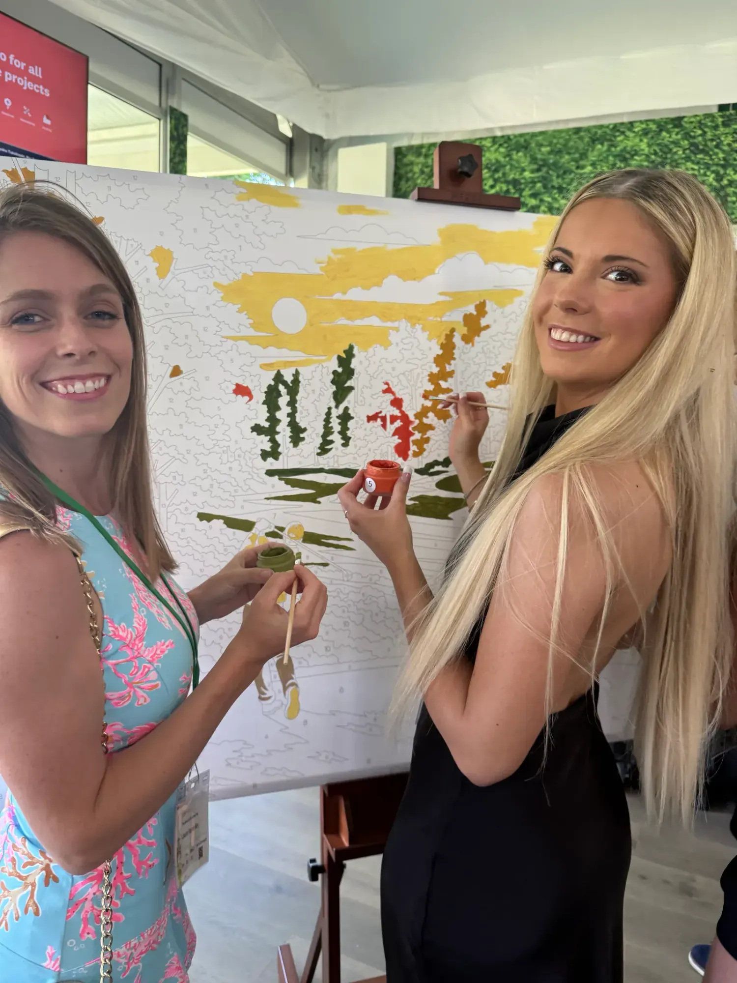 Two smiling guests painting numbered sections of a golf-themed paint-by-number mural